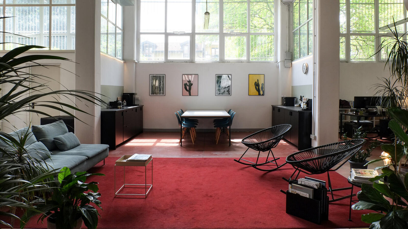 La lounge di C4 Workspace con tappeto rosso, divano salvia, piante e vetrate alte